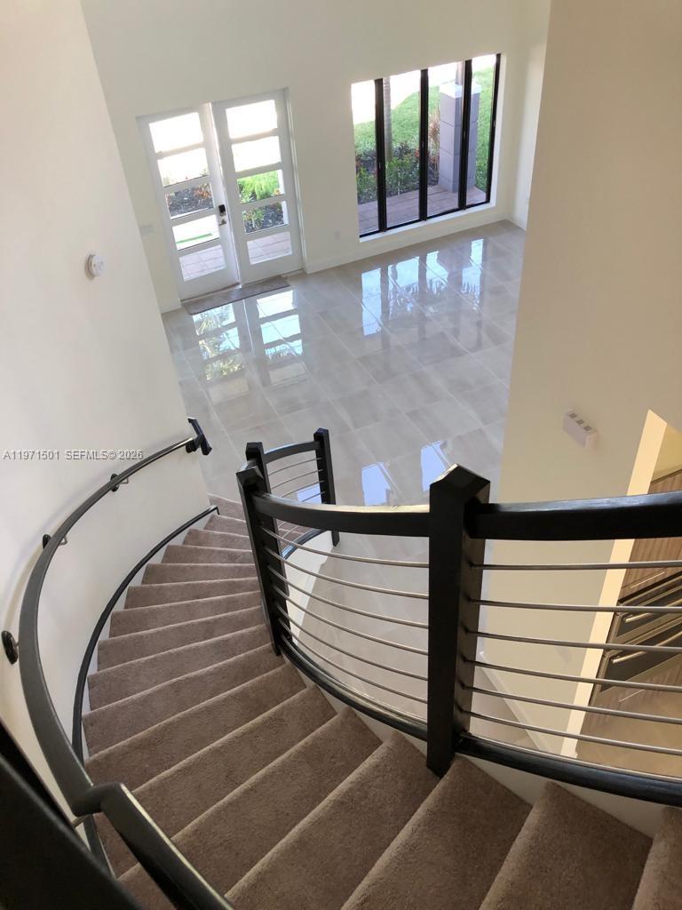 A curved staircase with carpeted steps and a metal railing overlooks a tiled foyer — 16045 NW 87th Ct, Miami Lakes FL 33018, MIAMI LAKES, FL