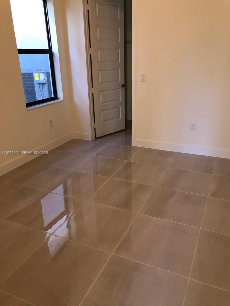 An empty room features large beige floor tiles, a window, and an open doorway — 16045 NW 87th Ct, Miami Lakes FL 33018, MIAMI LAKES, FL