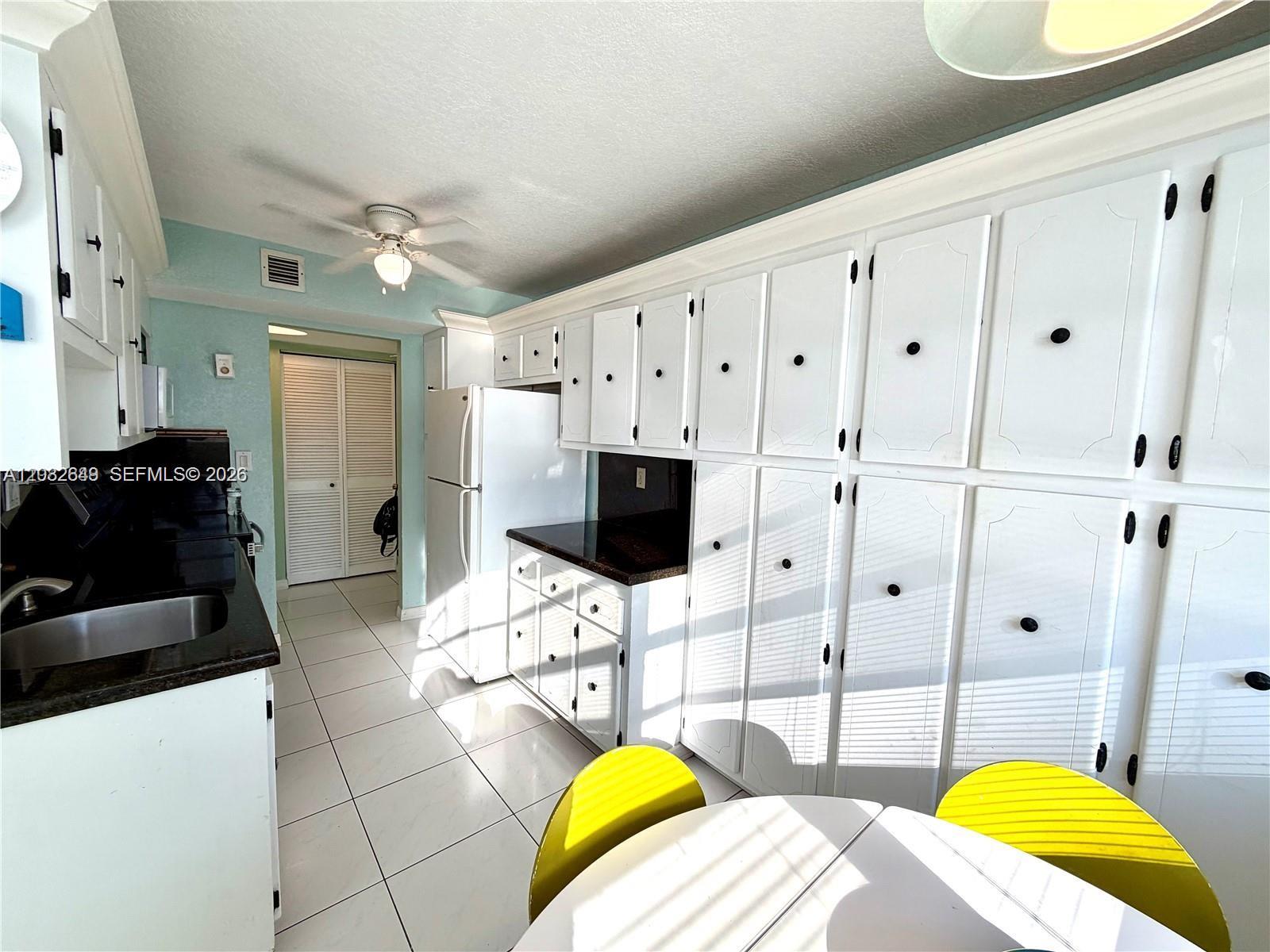 A kitchen features white cabinetry, black countertops, light blue walls, and white floor tiles — 1833 S Ocean Dr # 1202, Hallandale Beach FL 33009, HALLANDALE BEACH, FL