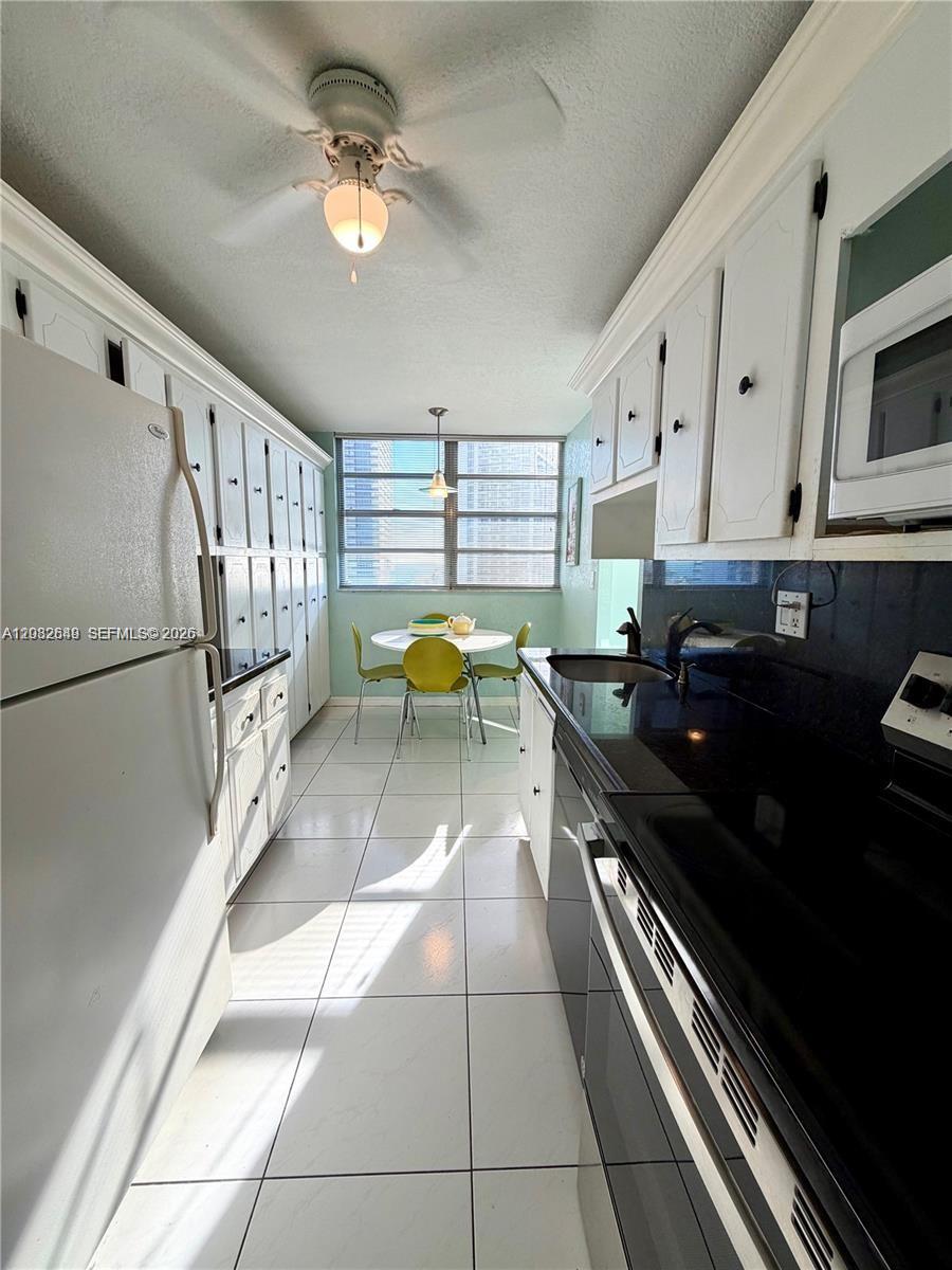 A galley kitchen features white cabinets, black countertops, and a small dining area by windows — 1833 S Ocean Dr # 1202, Hallandale Beach FL 33009, HALLANDALE BEACH, FL