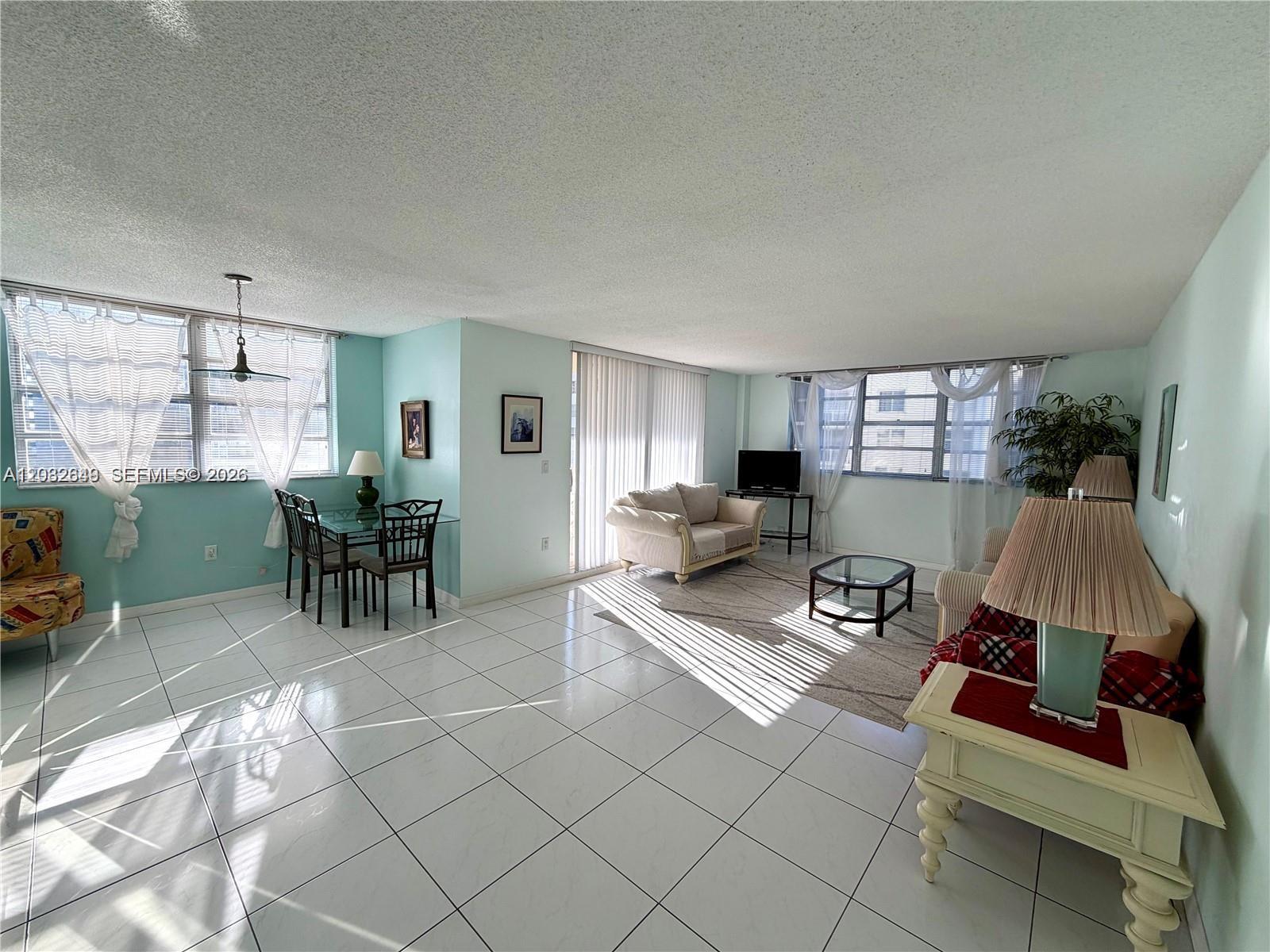 A bright, open-concept living and dining area features white tile flooring and light blue walls — 1833 S Ocean Dr # 1202, Hallandale Beach FL 33009, HALLANDALE BEACH, FL