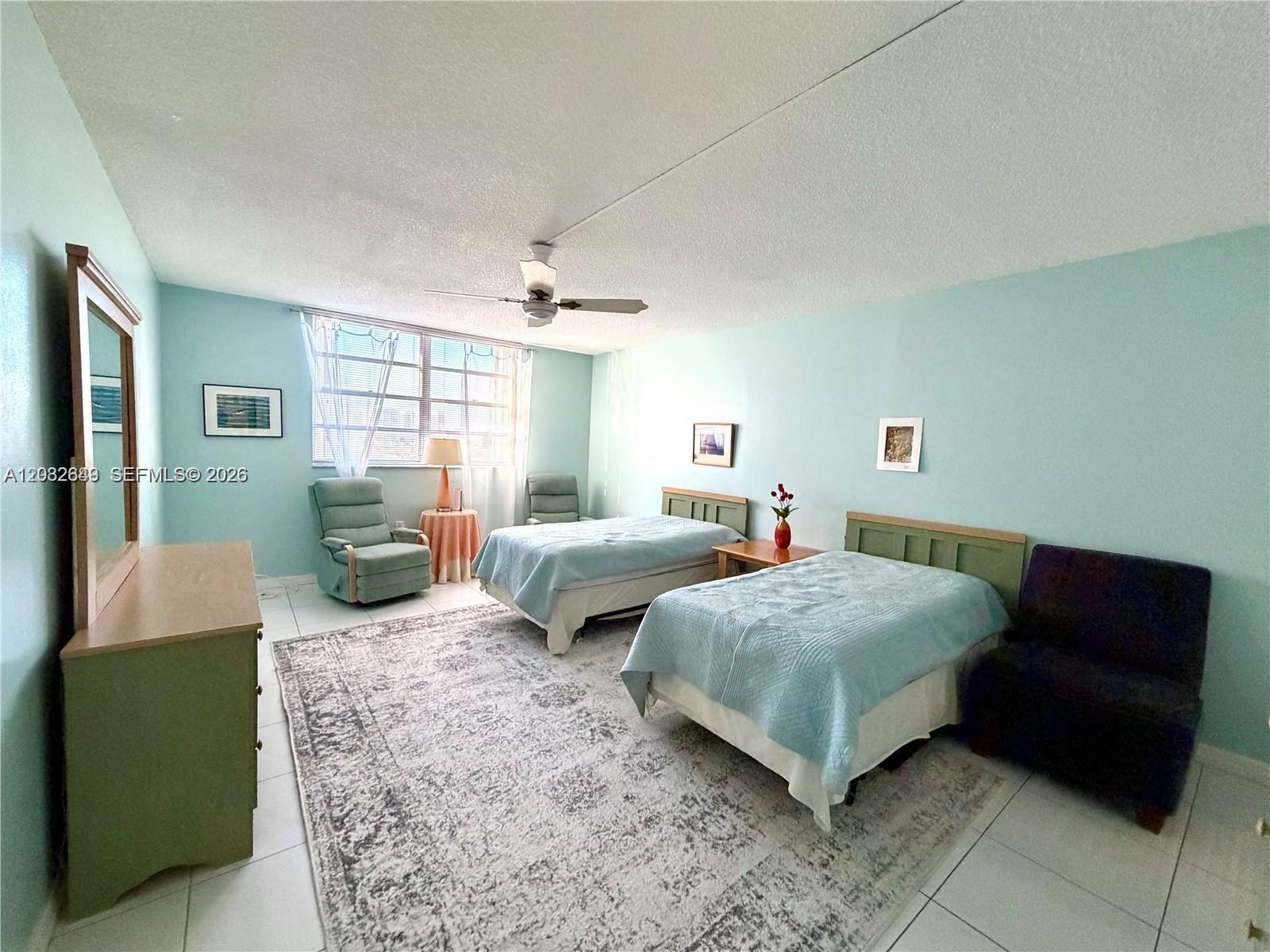 A bedroom features two twin beds, light blue walls, tile flooring, and a large rug — 1833 S Ocean Dr # 1202, Hallandale Beach FL 33009, HALLANDALE BEACH, FL