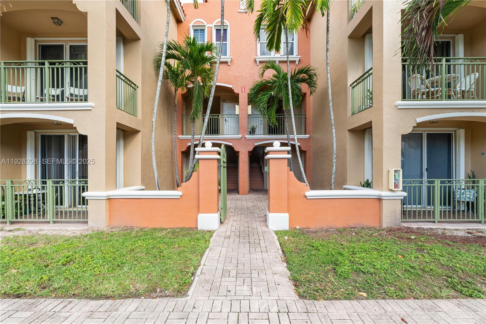 A paved walkway leads to the entrance of a multi-story orange stucco apartment building — 6500 NW 114th Ave # 1032, Doral FL 33178, DORAL, FL
