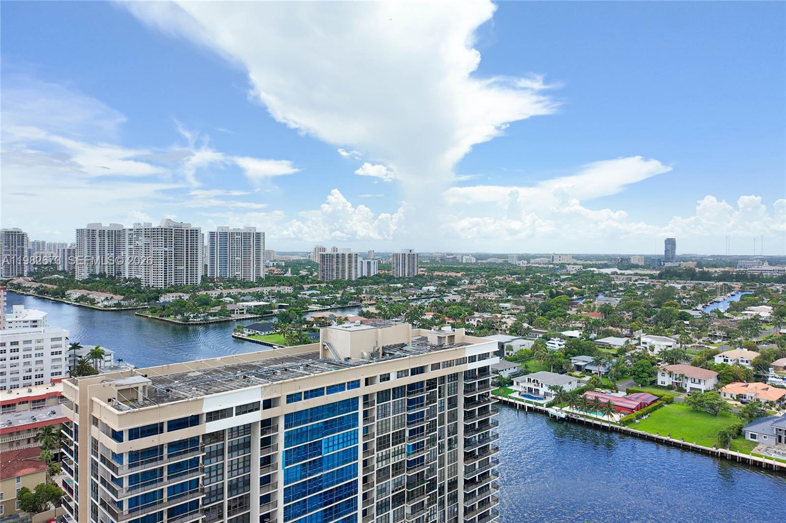 An aerial view shows a high-rise building overlooking a canal, residential homes, and distant skyscrapers — 1985 S Ocean Dr # 22E, Hallandale Beach FL 33009, HALLANDALE BEACH, FL