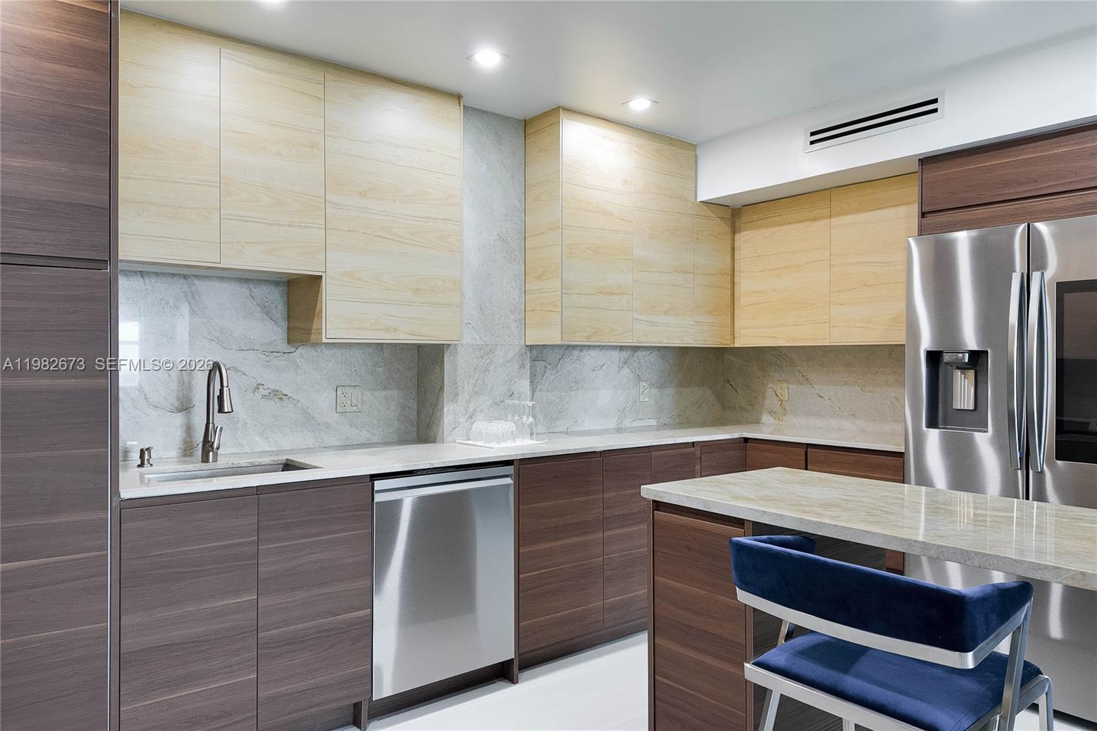 A modern kitchen features light wood upper cabinets, dark wood lower cabinets, and stone countertops — 1985 S Ocean Dr # 22E, Hallandale Beach FL 33009, HALLANDALE BEACH, FL