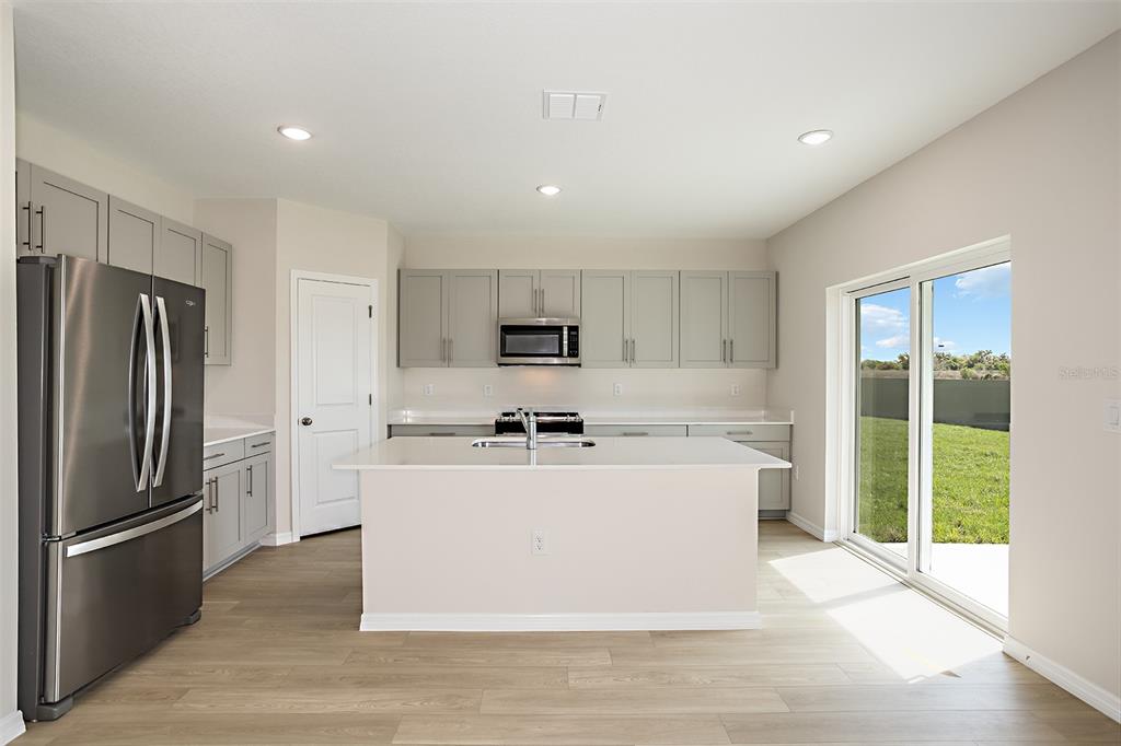 A modern kitchen features gray cabinets, stainless steel appliances, a white island, and sliding doors — 4418 RIVERBEND BOULEVARD, HAINES CITY, FL