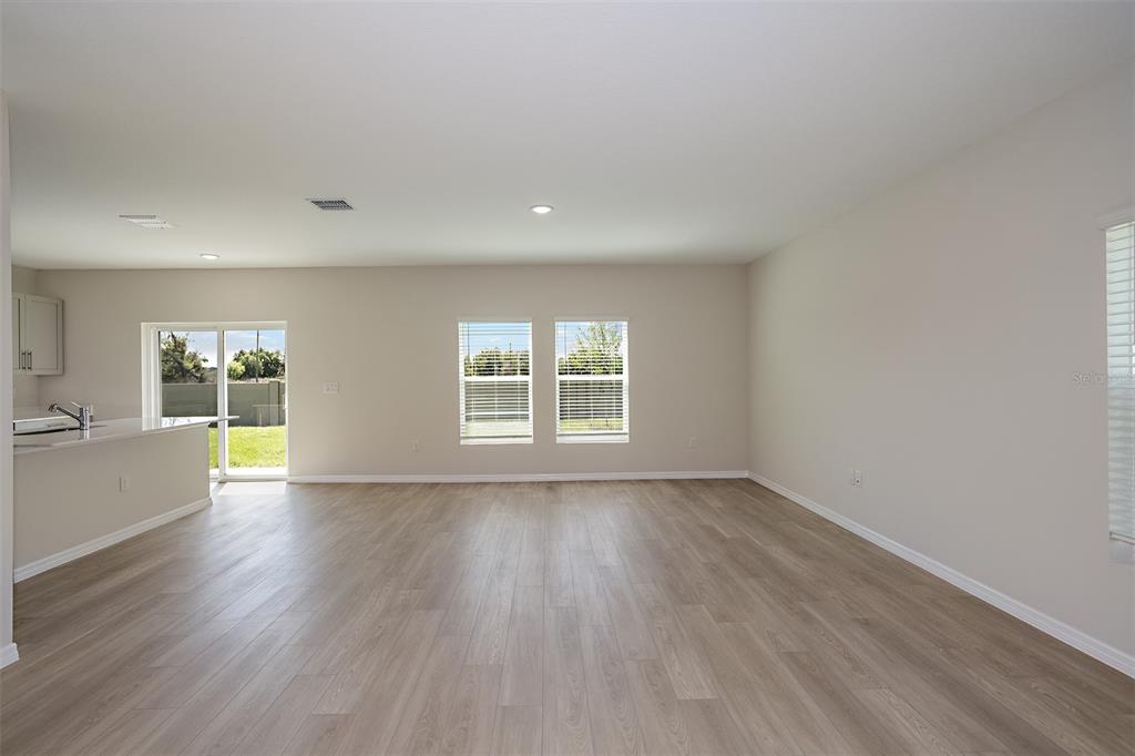 An open-concept living area with light wood-look flooring, neutral walls, and a sliding glass door — 4418 RIVERBEND BOULEVARD, HAINES CITY, FL