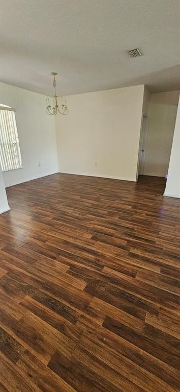 An empty room features wood-look laminate flooring, a chandelier, and a window with vertical blinds — 3905 BOWFIN TRAIL, KISSIMMEE, FL