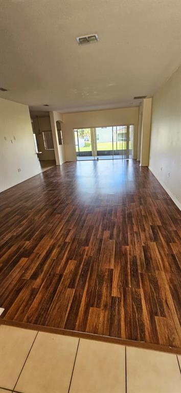 An empty living room features dark wood-look flooring and a large sliding glass door — 3905 BOWFIN TRAIL, KISSIMMEE, FL