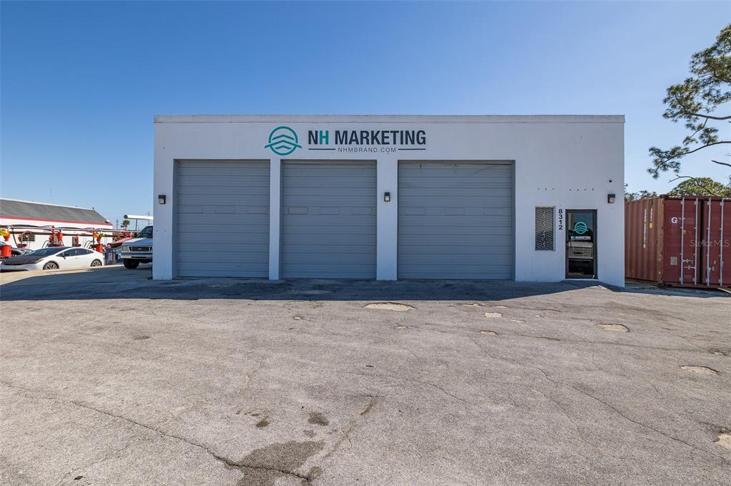 A white commercial building features three large gray garage doors and a single entrance door — 8312 US HIGHWAY 19, PORT RICHEY, FL