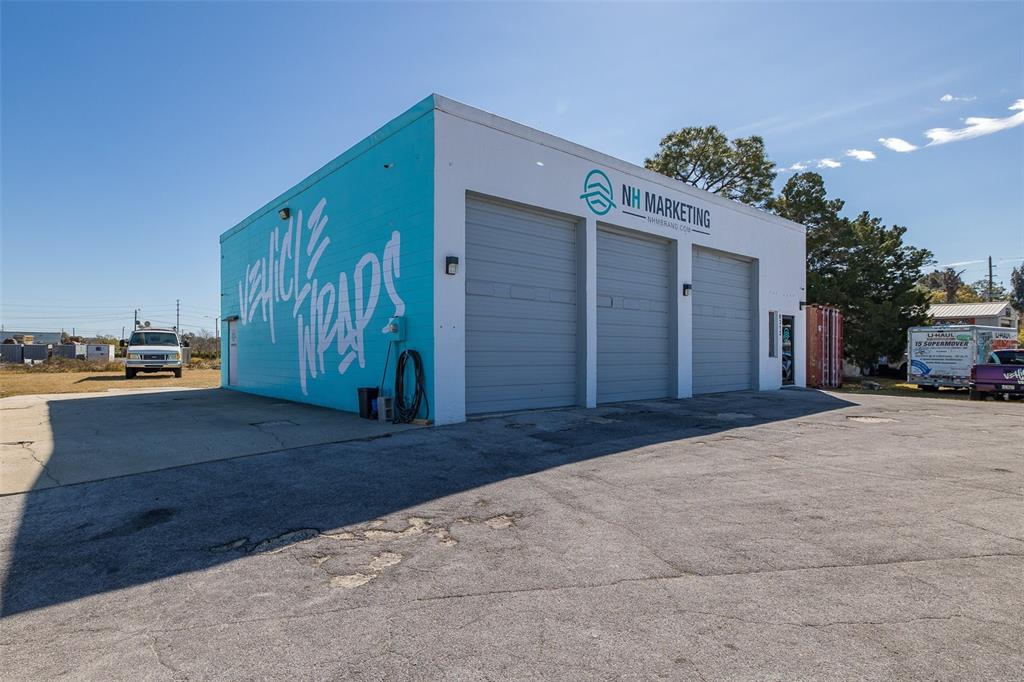 A commercial building with three garage doors and a blue wall painted with vehicle wraps — 8312 US HIGHWAY 19, PORT RICHEY, FL