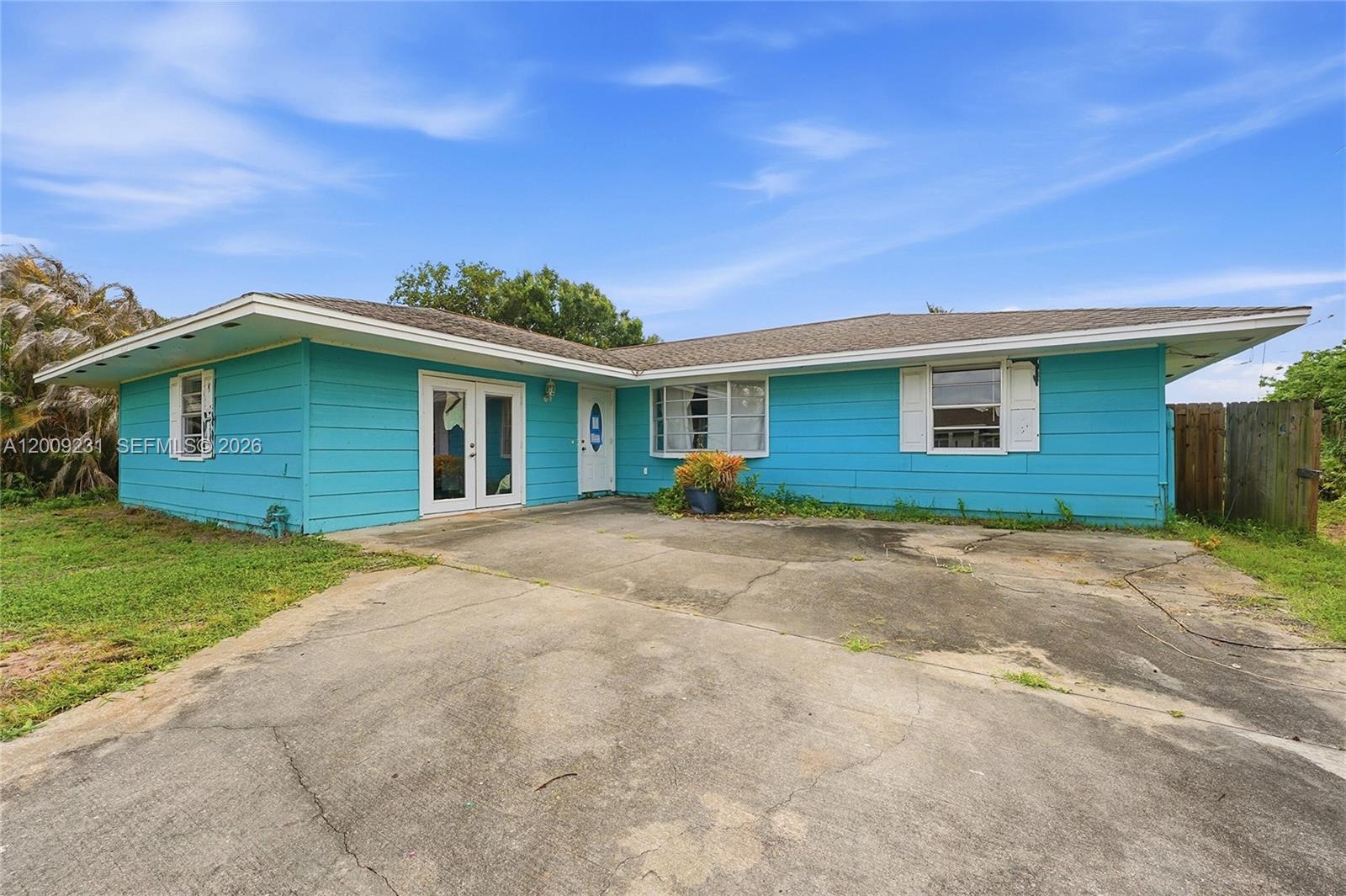 A single-story house with bright blue siding and a concrete driveway under a blue sky — 5808 Spruce Dr, Fort Pierce FL 34982, FORT PIERCE, FL