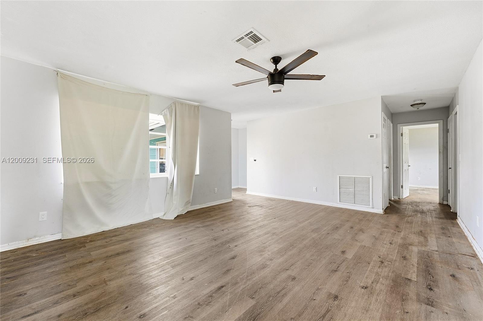 An empty room features light gray walls, wood-look flooring, a ceiling fan, and a window — 5808 Spruce Dr, Fort Pierce FL 34982, FORT PIERCE, FL