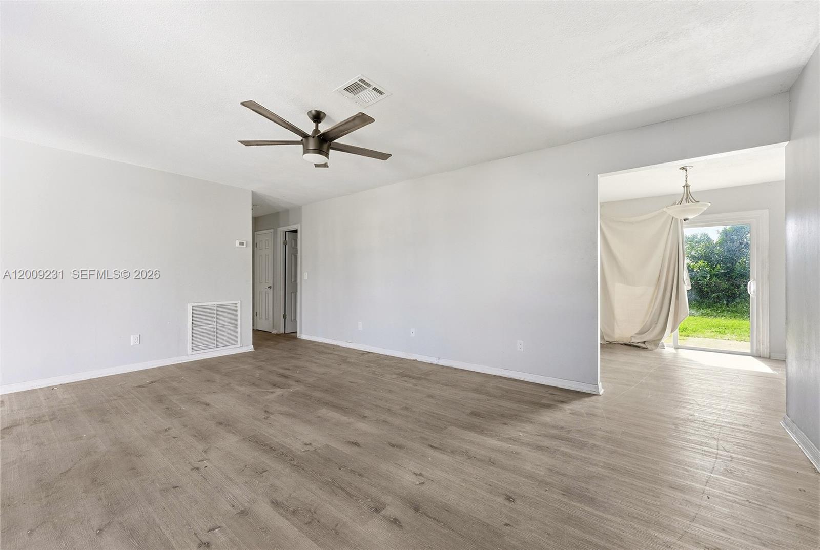 An empty room with light wood-look flooring, a ceiling fan, and a sliding glass door — 5808 Spruce Dr, Fort Pierce FL 34982, FORT PIERCE, FL