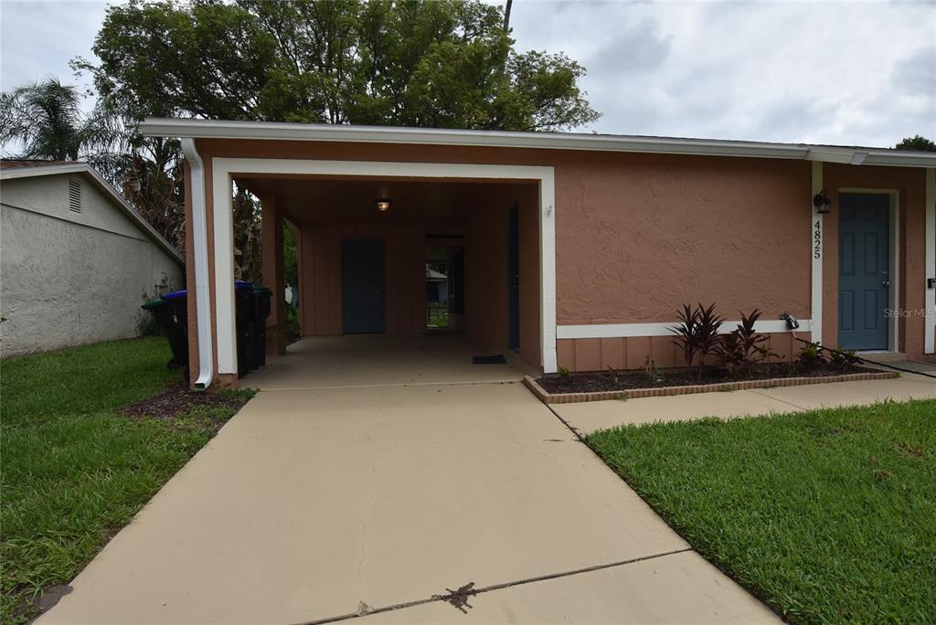 A tan house exterior features a concrete driveway leading to a covered carport and entrance — 4825 LORETTA LANE, ORLANDO, FL