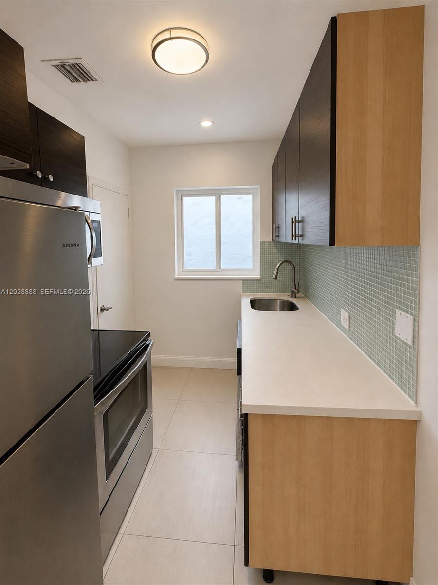 A galley kitchen features stainless steel appliances, light wood cabinets, and a light green backsplash — 1536 Jefferson Ave # 4, Miami Beach FL 33139, MIAMI BEACH, FL
