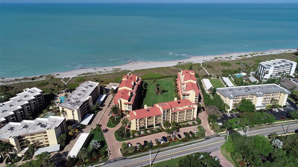 An aerial view shows several multi-story apartment buildings situated along a sandy beach — 8710 MIDNIGHT PASS ROAD UNIT 405, SARASOTA, FL