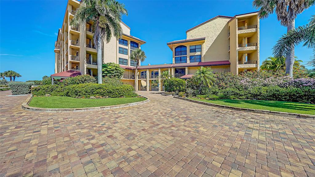 A paved driveway leads to the entrance of a multi-story, yellow-stucco resort building with palms — 8710 MIDNIGHT PASS ROAD UNIT 405, SARASOTA, FL