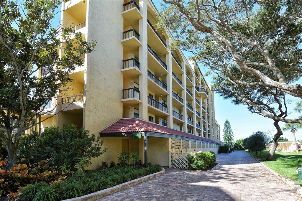 A multi-story yellow apartment building features balconies and a brick-paved driveway — 8710 MIDNIGHT PASS ROAD UNIT 405, SARASOTA, FL