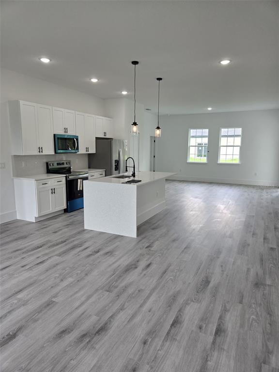 A modern kitchen features white cabinets, a central island, and light gray wood-look flooring — 4397 SW 169TH PLACE, OCALA, FL