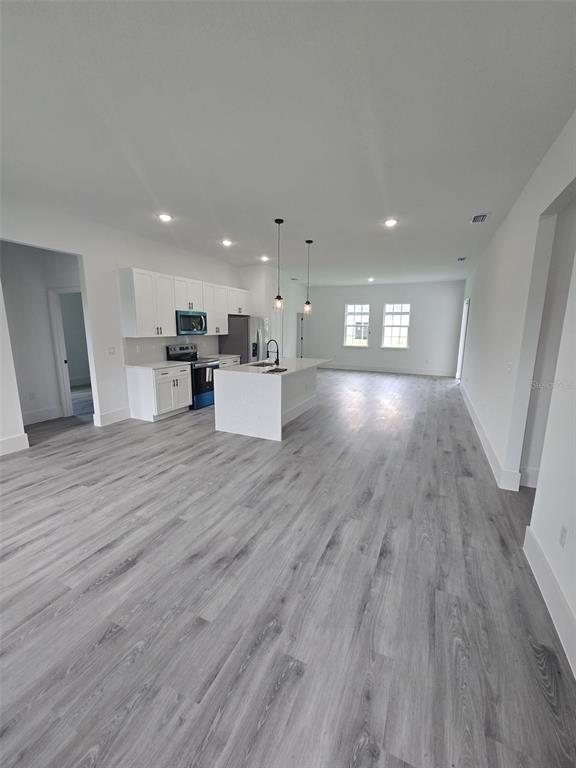 A modern kitchen with white cabinets and a center island features light gray wood flooring — 4397 SW 169TH PLACE, OCALA, FL