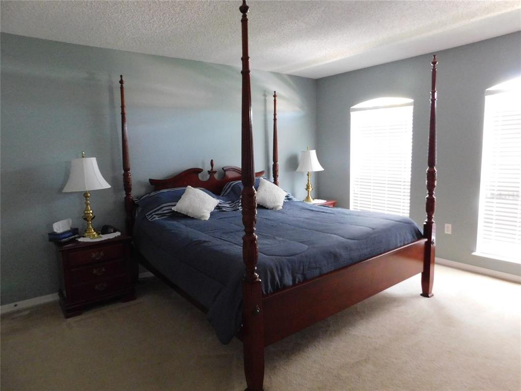 A bedroom features a dark wood four-poster bed, two nightstands with lamps, and blue walls — 2981 TOMORROW DRIVE, KISSIMMEE, FL