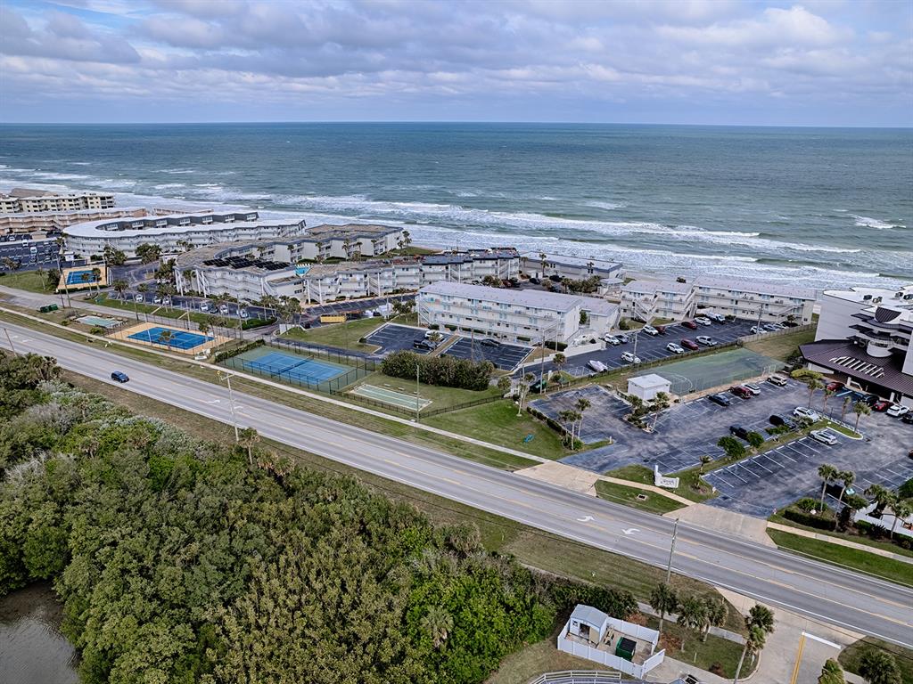 An aerial view shows a coastal resort complex with tennis courts, parking, and oceanfront buildings — 4870 S. ATLANTIC AVE, UNIT 2040, NEW SMYRNA BEACH, FL