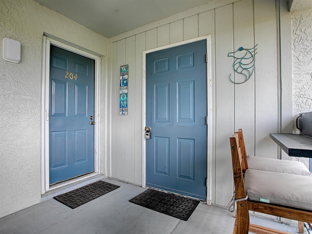 Two blue doors with welcome signage and a small patio area with a wooden chair — 4870 S. ATLANTIC AVE, UNIT 2040, NEW SMYRNA BEACH, FL