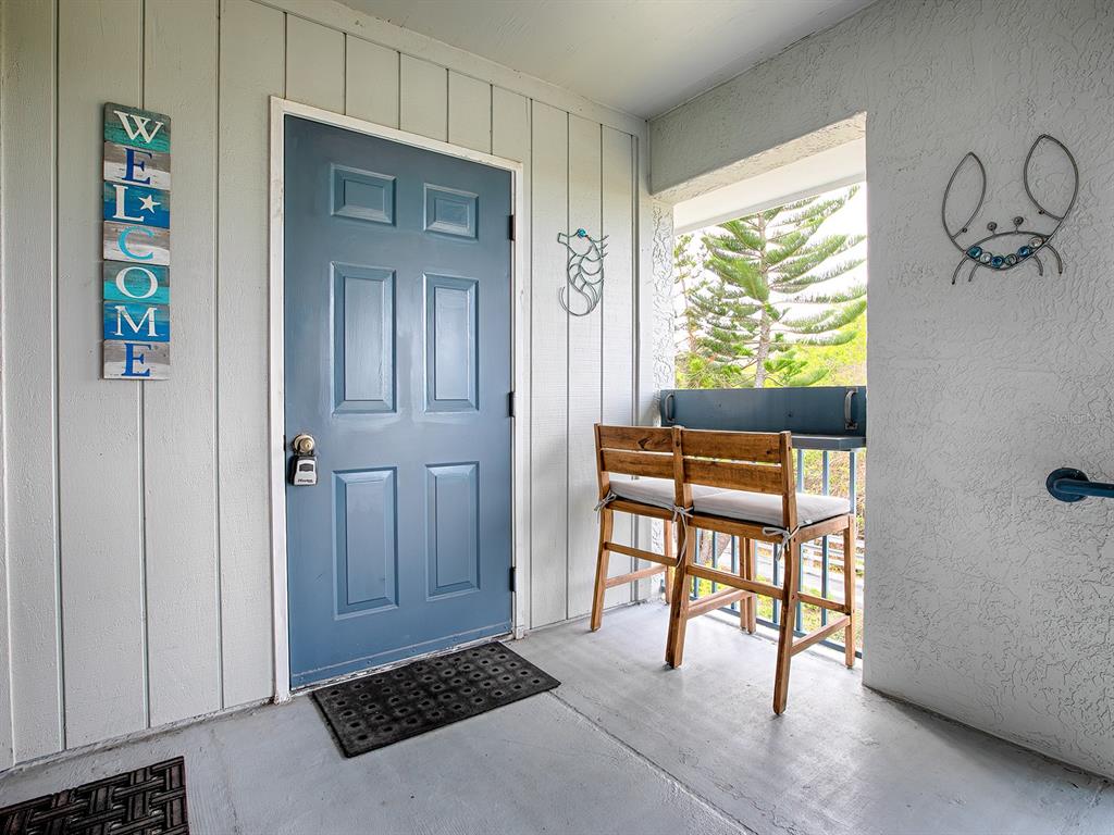 A blue front door sits next to a small balcony with two wooden bar stools — 4870 S. ATLANTIC AVE, UNIT 2040, NEW SMYRNA BEACH, FL