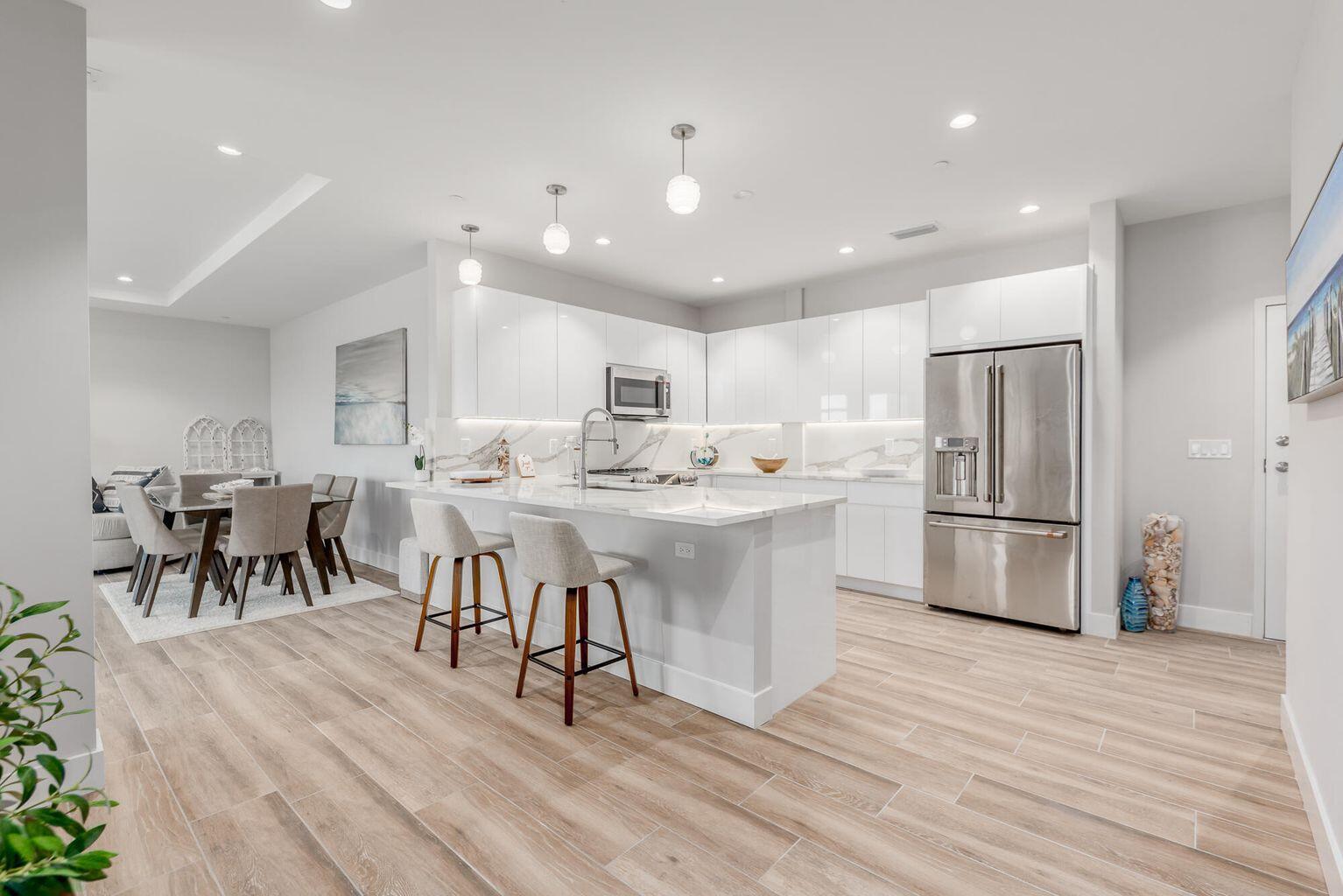 A modern kitchen features white cabinets, a marble island with bar stools, and light wood flooring — 41 SW Seminole Street # 410, Stuart FL 34994, STUART, FL