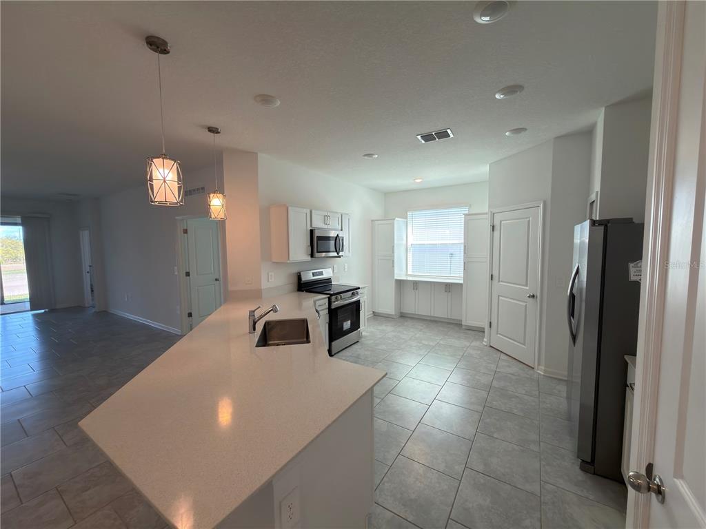 An open-concept kitchen features a white island, stainless steel appliances, and light-colored tile flooring — 521 REGGIE ROAD, WINTER HAVEN, FL