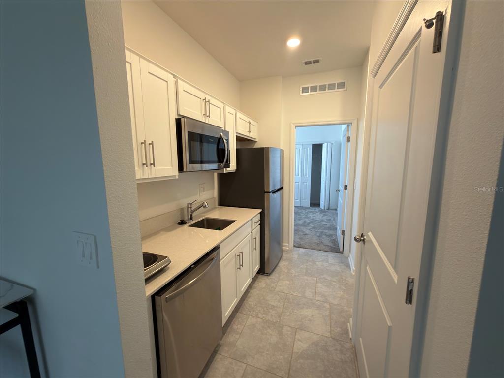 A small kitchen features white cabinets, stainless steel appliances, and light-colored countertops — 521 REGGIE ROAD, WINTER HAVEN, FL
