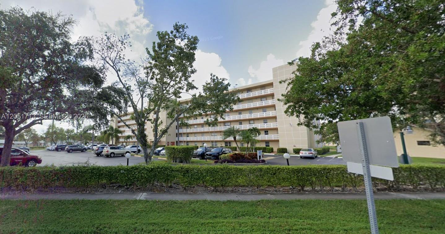 A multi-story apartment building with balconies stands behind a parking lot and manicured hedges — 441 SE 3rd St # 505, Dania Beach FL 33004, DANIA BEACH, FL