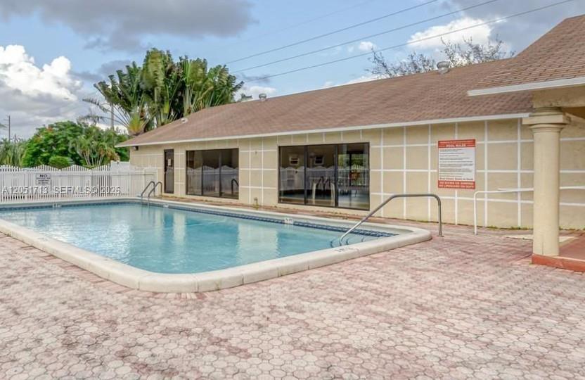 A rectangular swimming pool sits on a paved patio beside a tan building with sliding doors — 441 SE 3rd St # 505, Dania Beach FL 33004, DANIA BEACH, FL