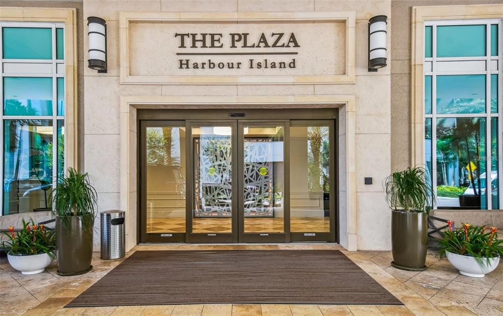The exterior entrance of The Plaza Harbour Island features sliding glass doors and potted plants — 450 KNIGHTS RUN AVENUE UNIT 102, TAMPA, FL