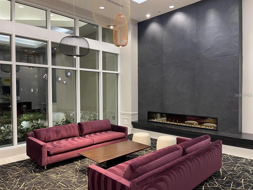 A modern lounge area features two purple velvet sofas, a fireplace, and large windows — 450 KNIGHTS RUN AVENUE UNIT 102, TAMPA, FL