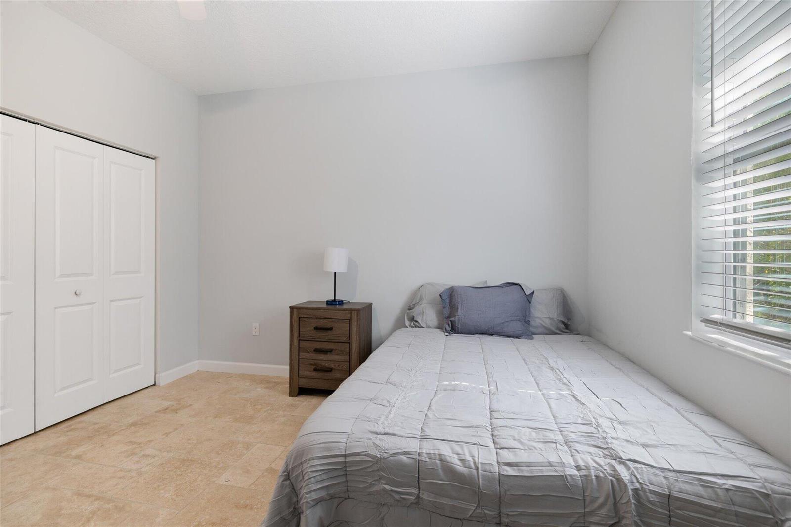 A bedroom with light-colored walls, tile flooring, a bed, a nightstand, and a closet — VERO BEACH, FL