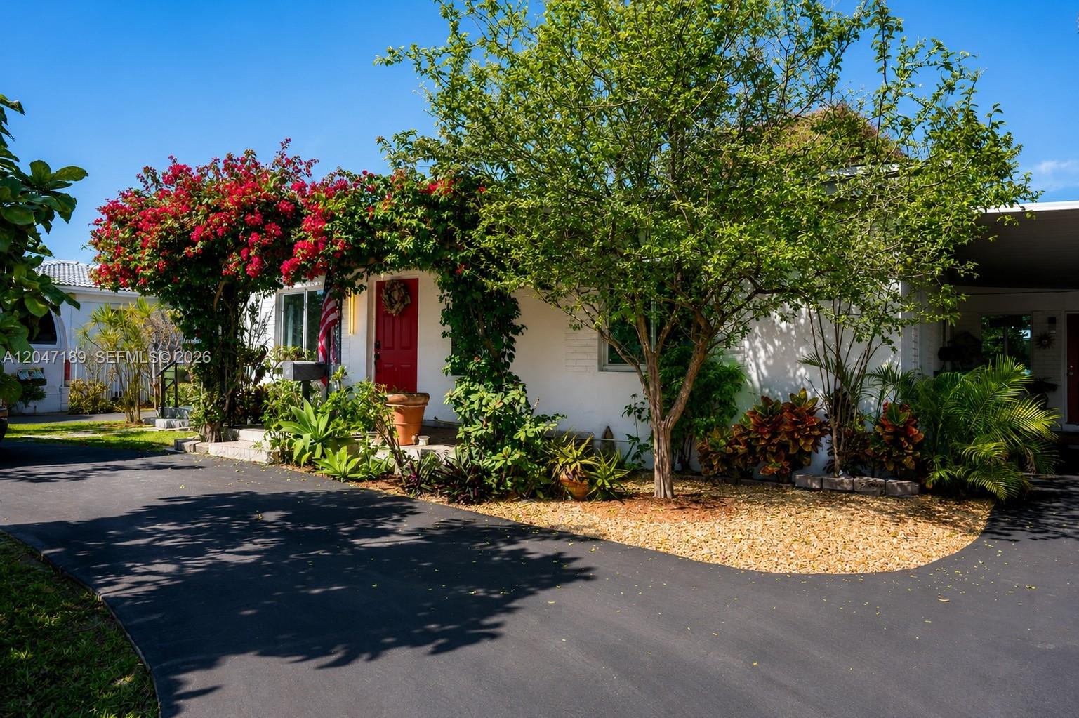 A white house with a red door and a large bougainvillea bush by the driveway — 861 W 32nd St, Hialeah FL 33012, HIALEAH, FL