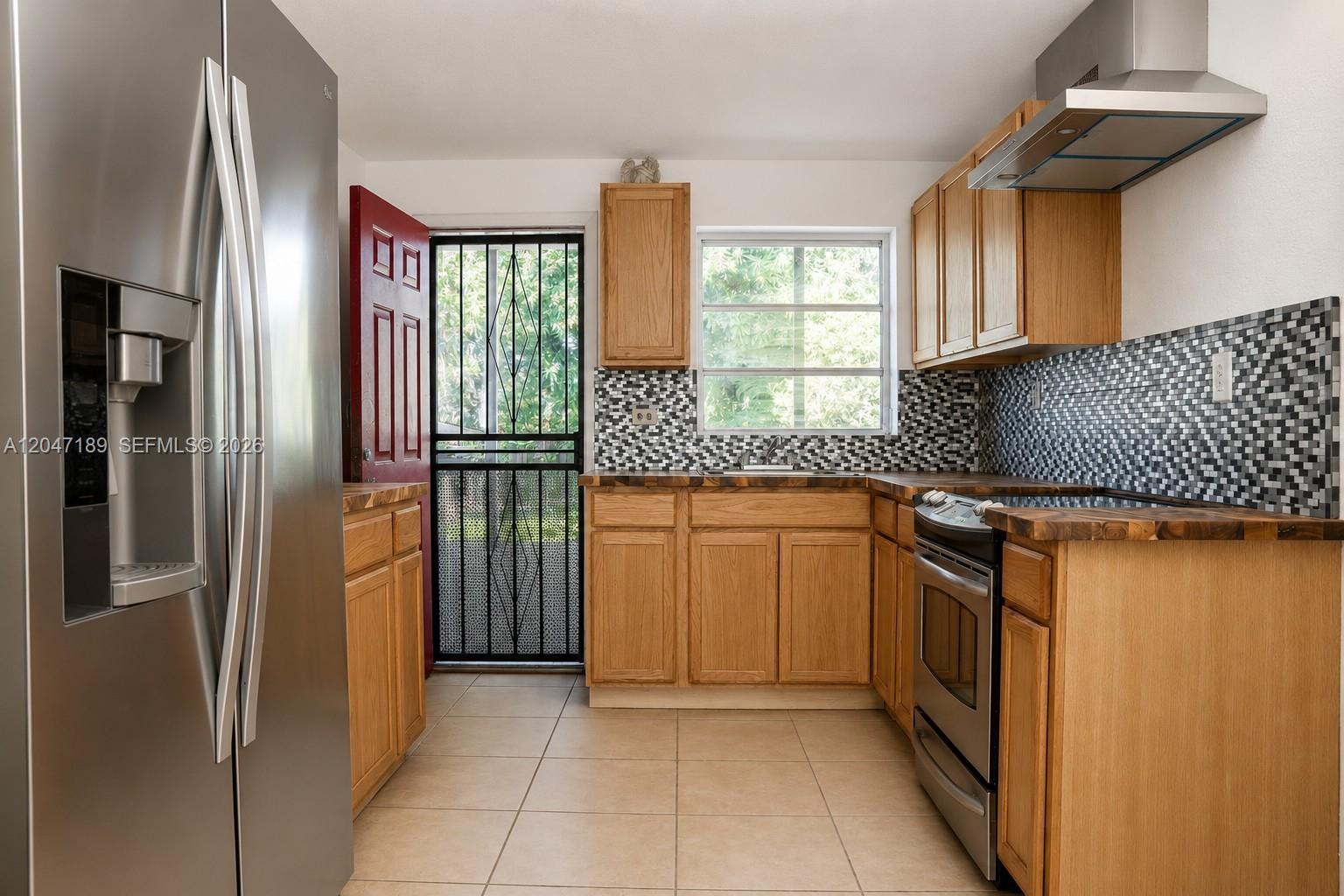 A kitchen features wood cabinets, stainless steel appliances, a mosaic tile backsplash, and a door — 861 W 32nd St, Hialeah FL 33012, HIALEAH, FL