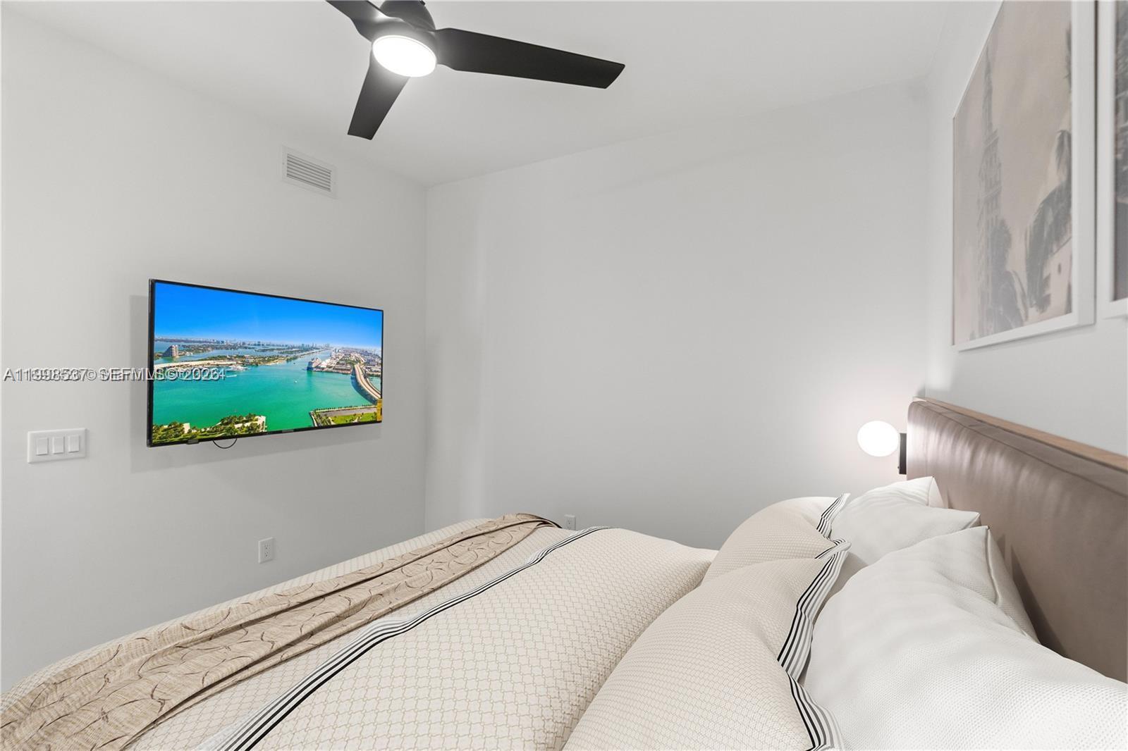 A bedroom features a wall-mounted television, a ceiling fan, and a bed with neutral bedding — 159 NE 6th St # 2403, Miami FL 33132, MIAMI, FL