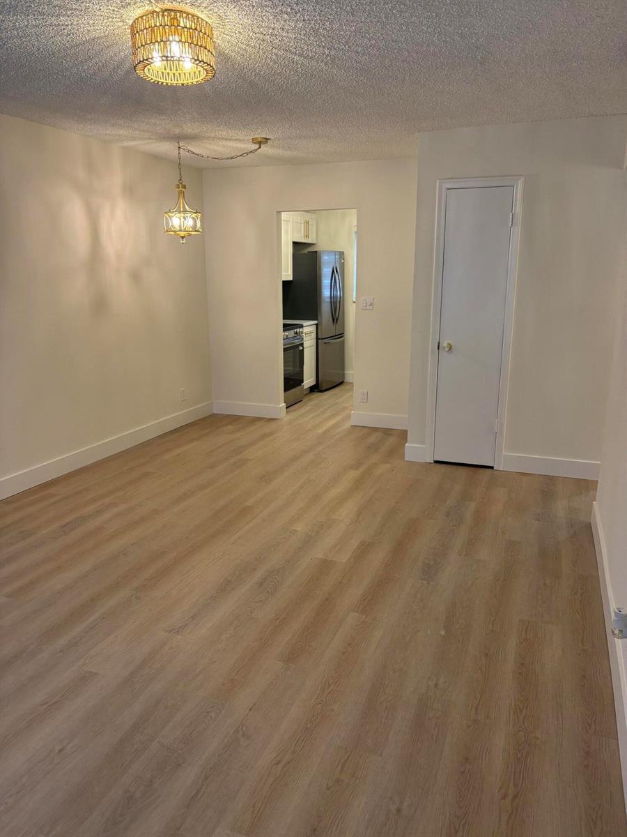 A dining area with light wood-look flooring, a hanging pendant light, and a kitchen doorway — 1230 Old Boynton Road # 208, Boynton Beach FL 33426, BOYNTON BEACH, FL