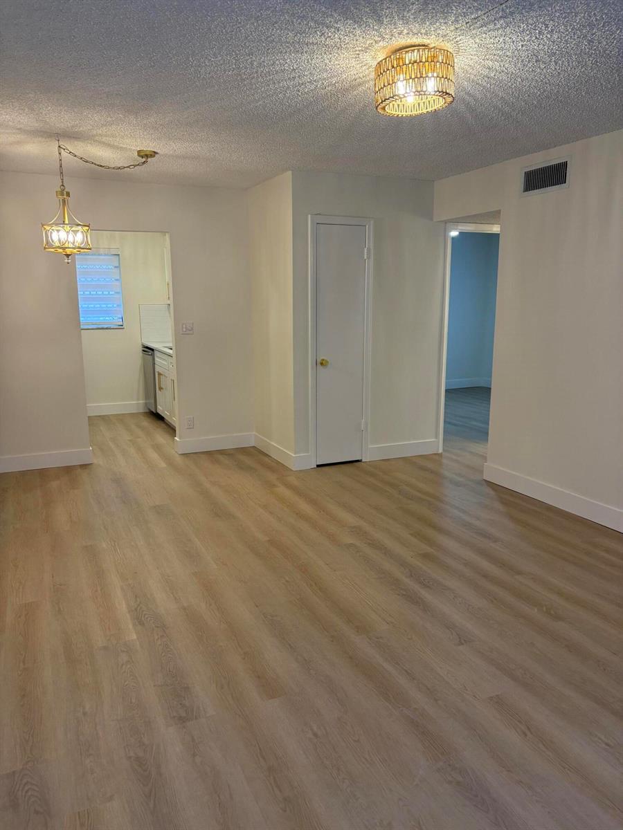 A living area with light wood-look flooring, white walls, and two overhead light fixtures — 1230 Old Boynton Road # 208, Boynton Beach FL 33426, BOYNTON BEACH, FL