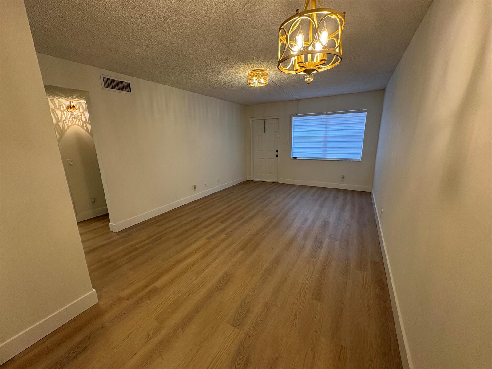 An empty living room features light wood-look flooring, white walls, and two gold light fixtures — 1230 Old Boynton Road # 208, Boynton Beach FL 33426, BOYNTON BEACH, FL
