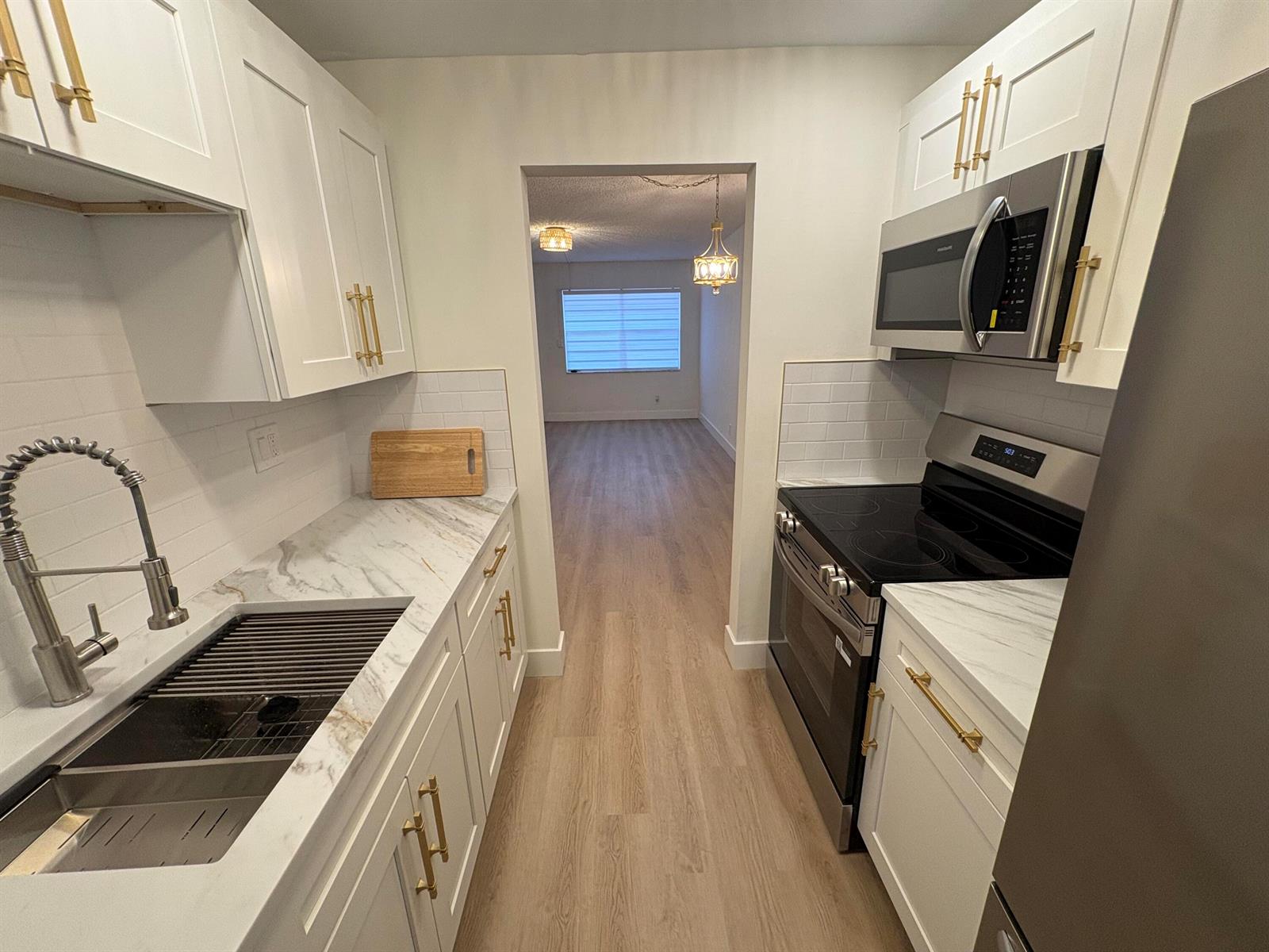 A galley kitchen features white cabinets, gold hardware, marble-look countertops, and stainless steel appliances — 1230 Old Boynton Road # 208, Boynton Beach FL 33426, BOYNTON BEACH, FL