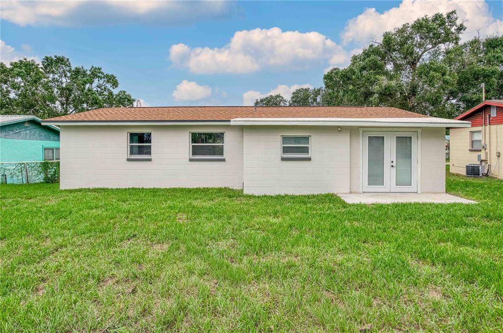 The back exterior of a single-story white house with a lawn and double glass doors — 717 W WINIFRED STREET, AVON PARK, FL