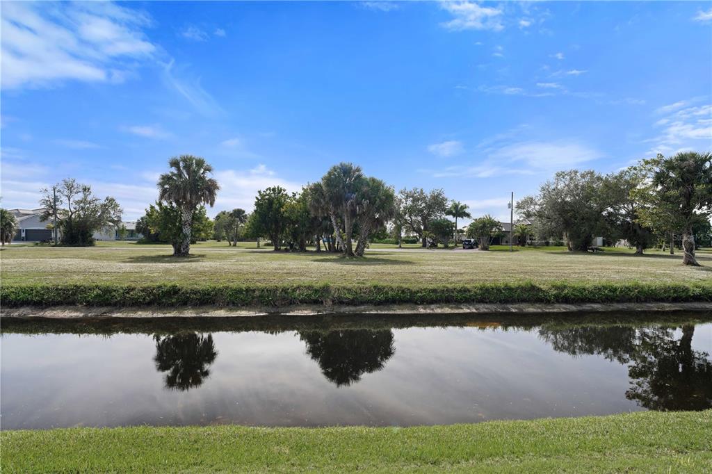A grassy field with palm trees sits behind a narrow canal under a blue sky — 17157 MINT LANE, PUNTA GORDA, FL
