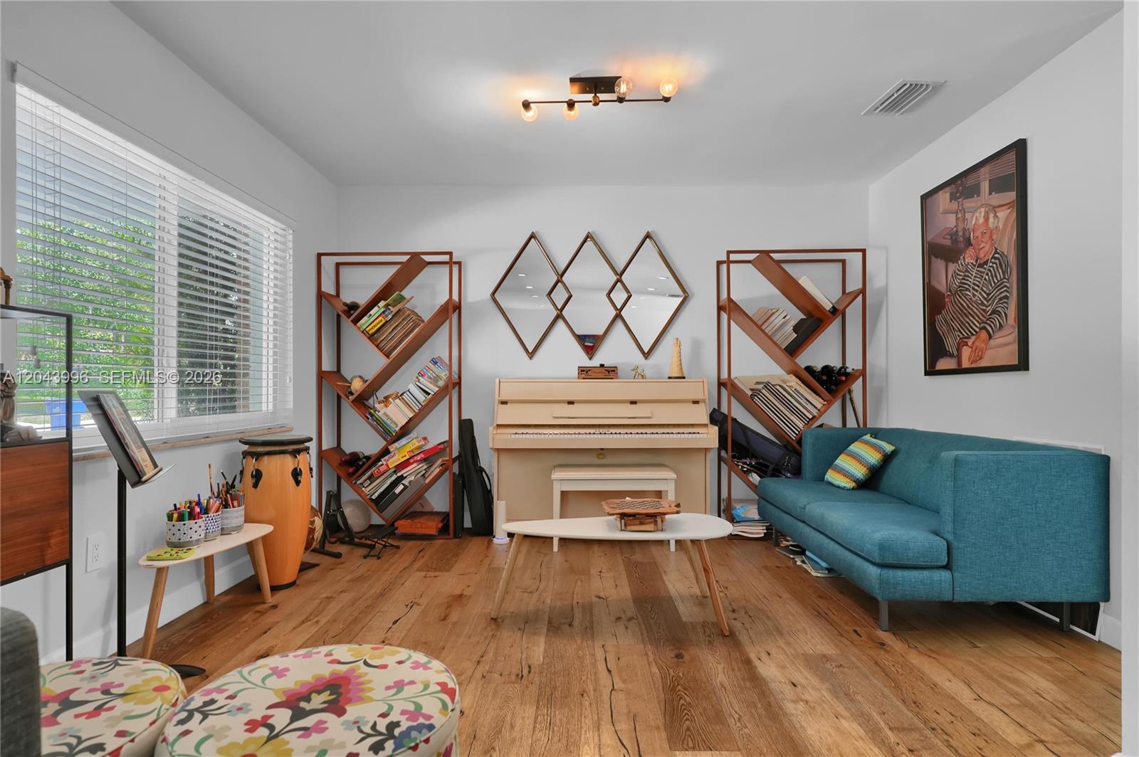 A living room features a piano, two wooden bookshelves, a teal sofa, and wood flooring — 5721 SW 59th Ct, South Miami FL 33143, SOUTH MIAMI, FL