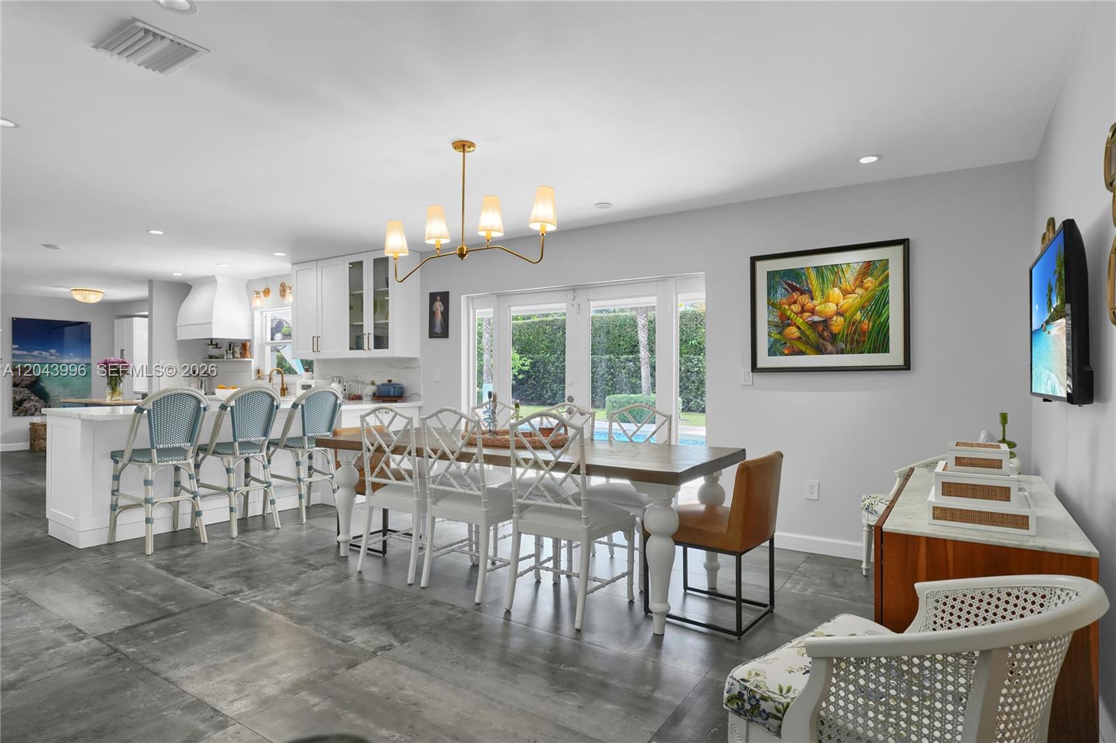A dining area with a wooden table, white chairs, and a kitchen island with stools — 5721 SW 59th Ct, South Miami FL 33143, SOUTH MIAMI, FL