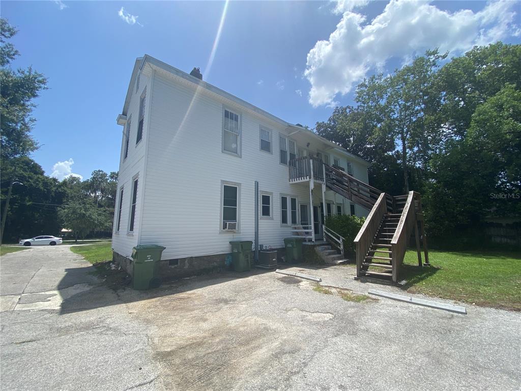 A two-story white building features an exterior wooden staircase leading to the second floor — 1120 WEBSTER STREET UNIT 4, LEESBURG, FL
