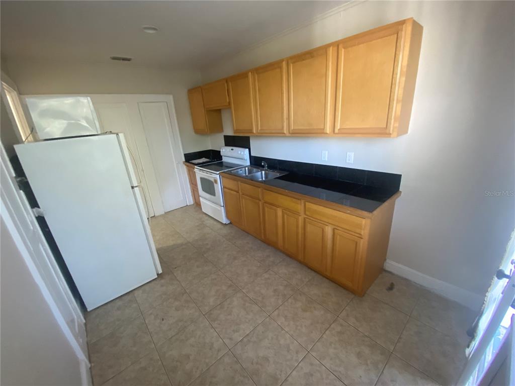 A kitchen features light wood cabinets, black countertops, a white refrigerator, and tiled flooring — 1120 WEBSTER STREET UNIT 4, LEESBURG, FL